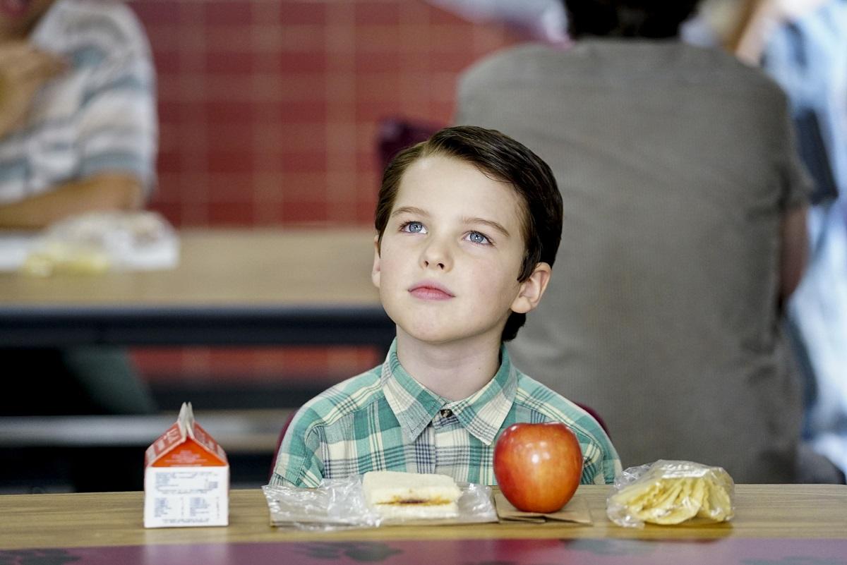 Iain Armitage as Sheldon Cooper wears a green shirt in the lunchroom during an episode of